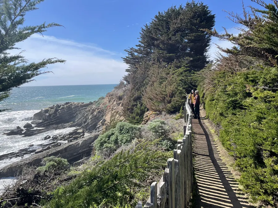 Two walkers on the bluff-top trail at Gualala Point, with surf breaking on the rocks below